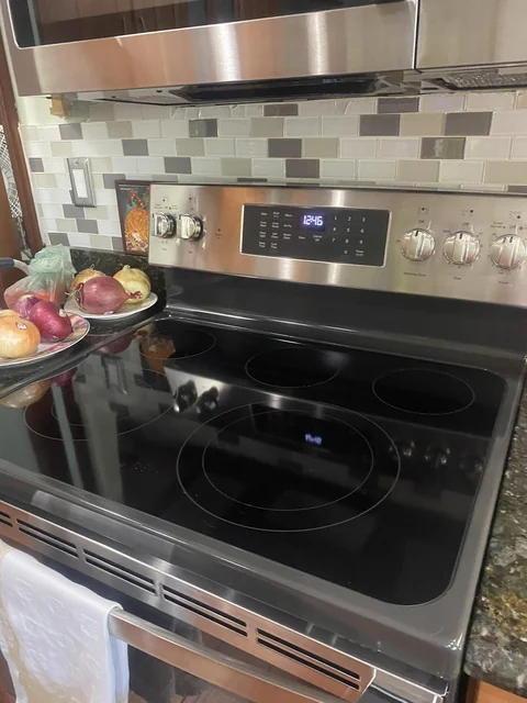 A clean black glass stovetop and stainless steel range