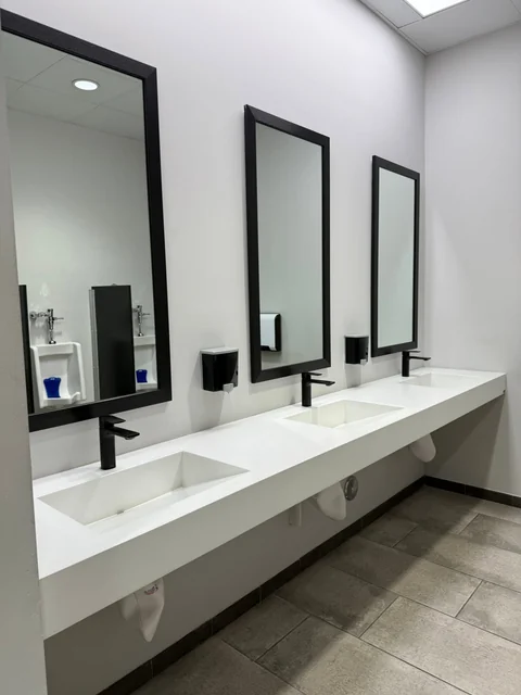 A long white washroom vanity with three mirrors and black fixtures